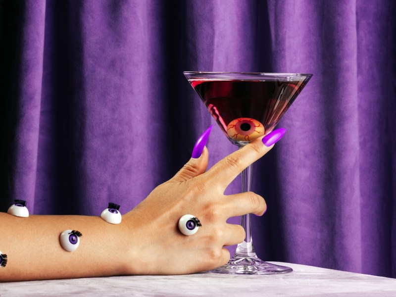 Frau hält ein Martini-Glas mit einem Halloween-Augapfel darin.