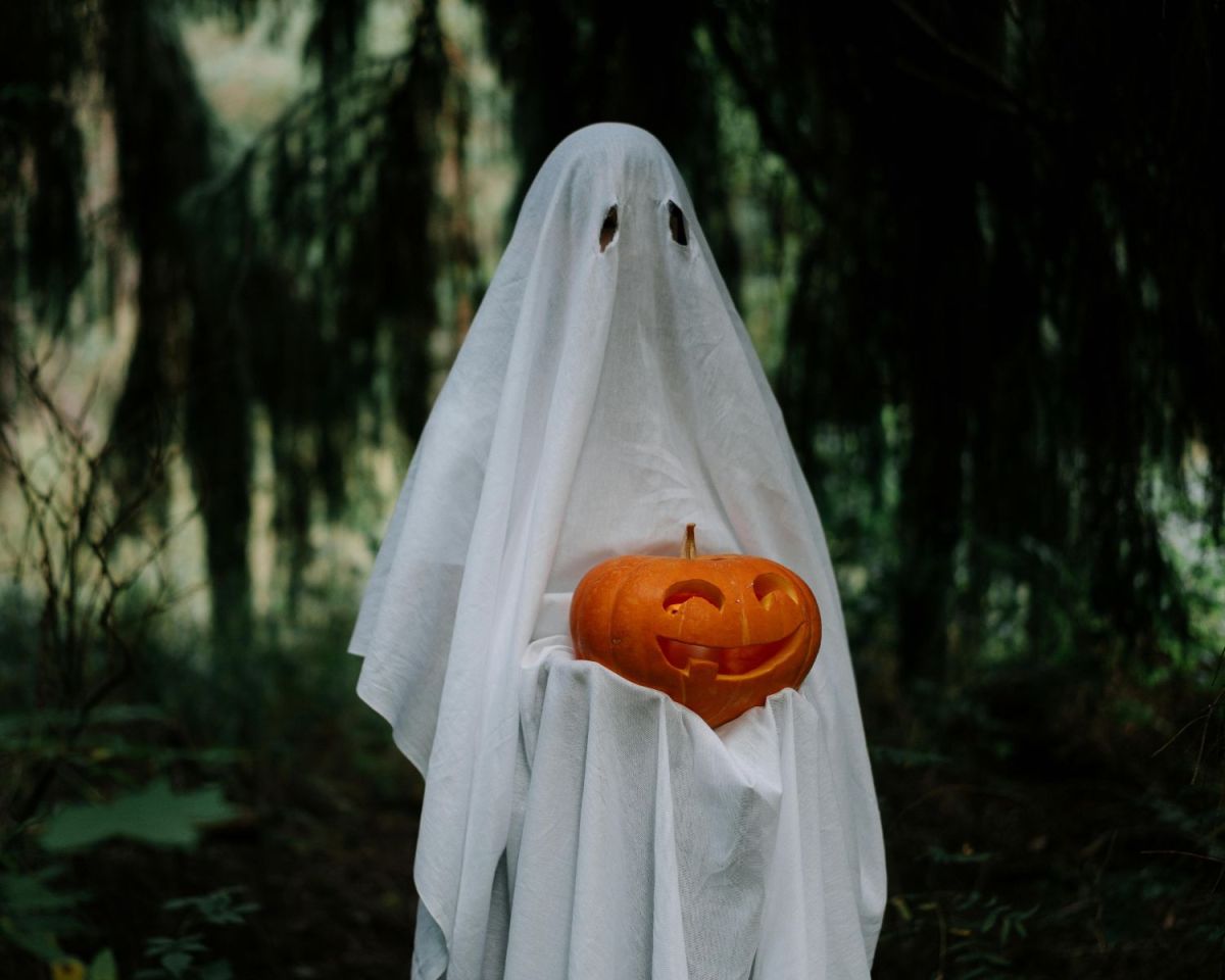 Halloween-Kostüm als Geist mit einem geschnitzten Kürbis in der Hand
