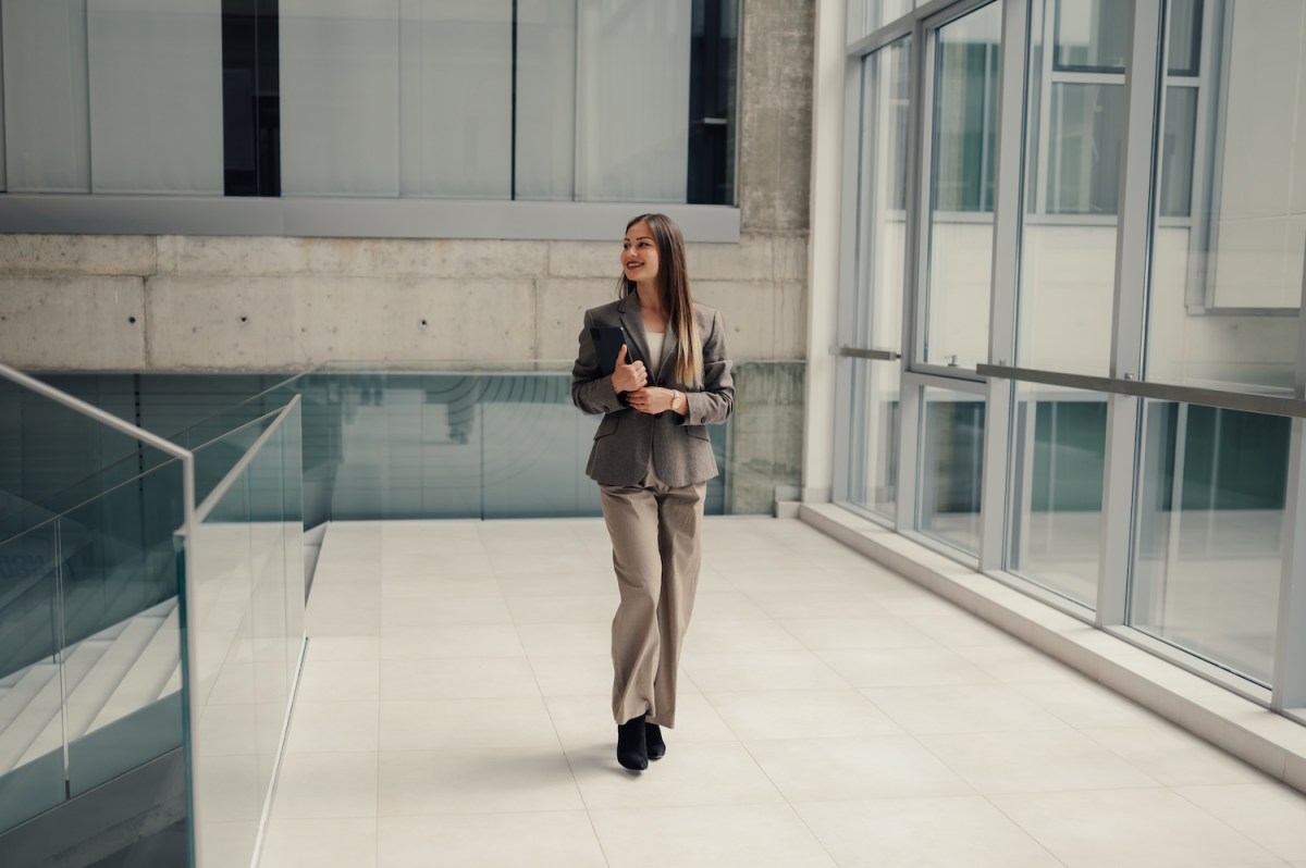 Selbstbewusste Geschäftsfrau, die mit einem Tablet durch ein modernes Bürogebäude geht.