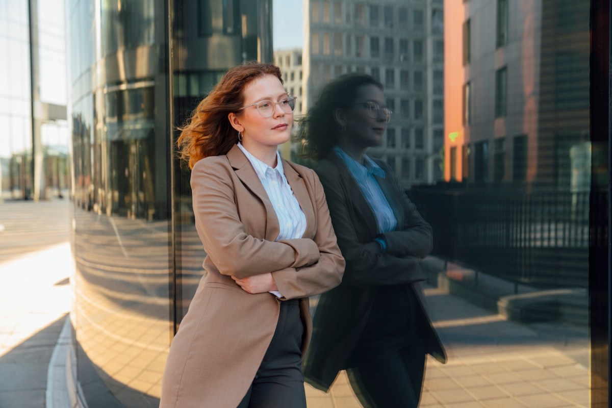 Nachdenkliche Geschäftsfrau stützte sich auf Bürogebäude mit Reflexion.