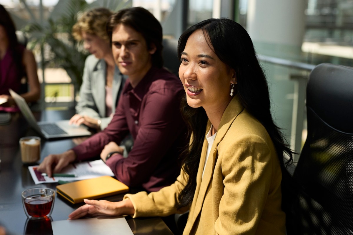 Eine Frau sitzt im Meeting und lächelt.