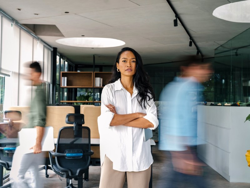 Eine Frau steht selbstbewusst im Büro.