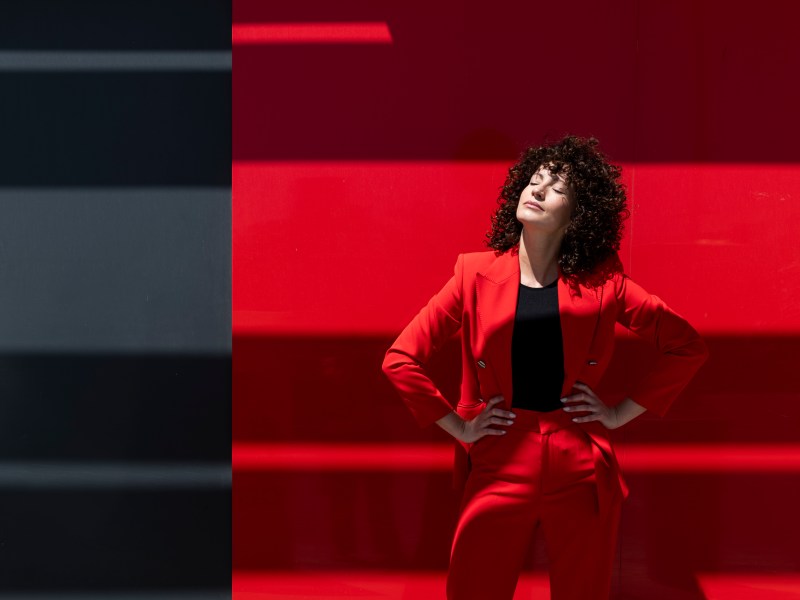 Geschäftsfrau im roten Anzug steht mit geschlossenen Augen vor einer Wand.