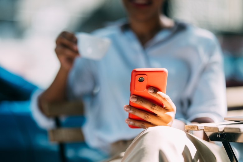 Eine Frau hält ein orangenes Handy in der Hand.