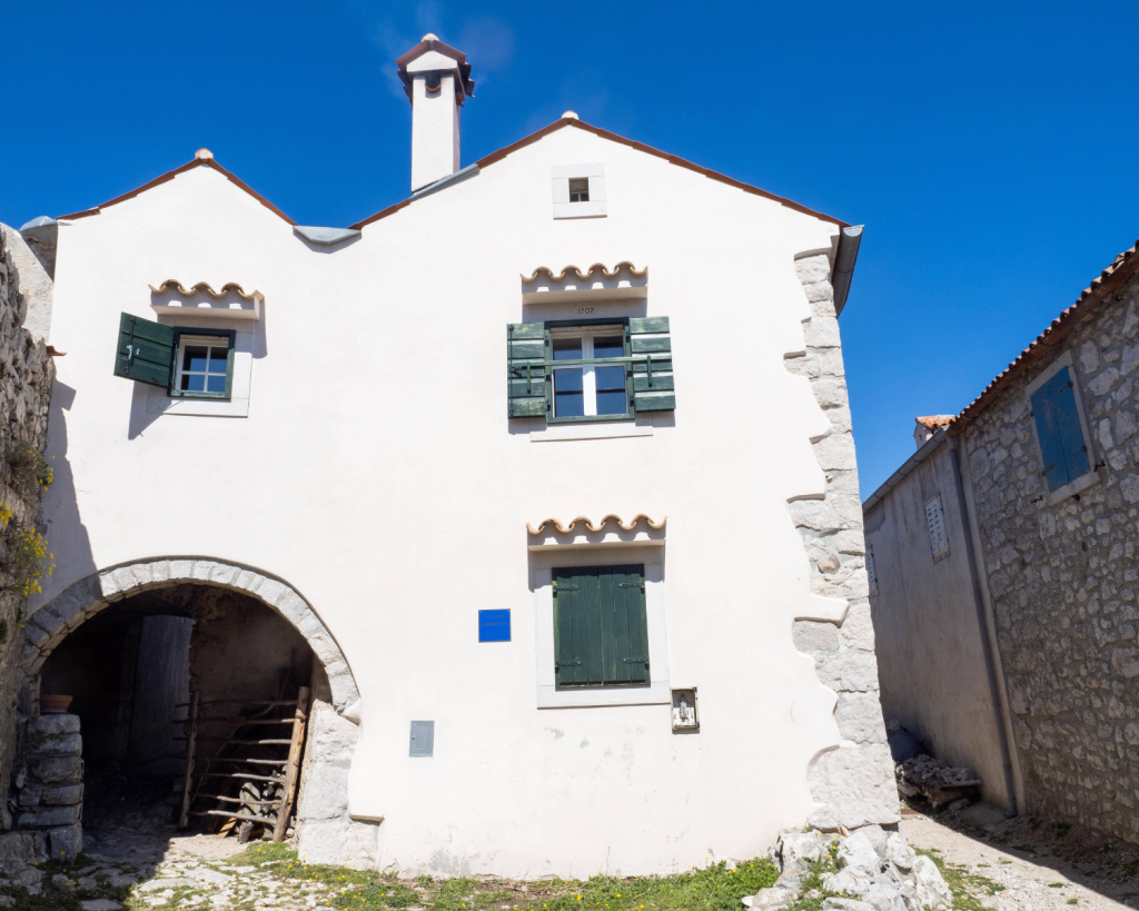 Das Haus befindet sich auf Lubenice. Hierbei handelt es sich um den älteste Siedlungsplatz auf Cres, sehr prominent gelegen auf einer 375 m hohen, steil über dem Meer aufragenden Felskanzel.