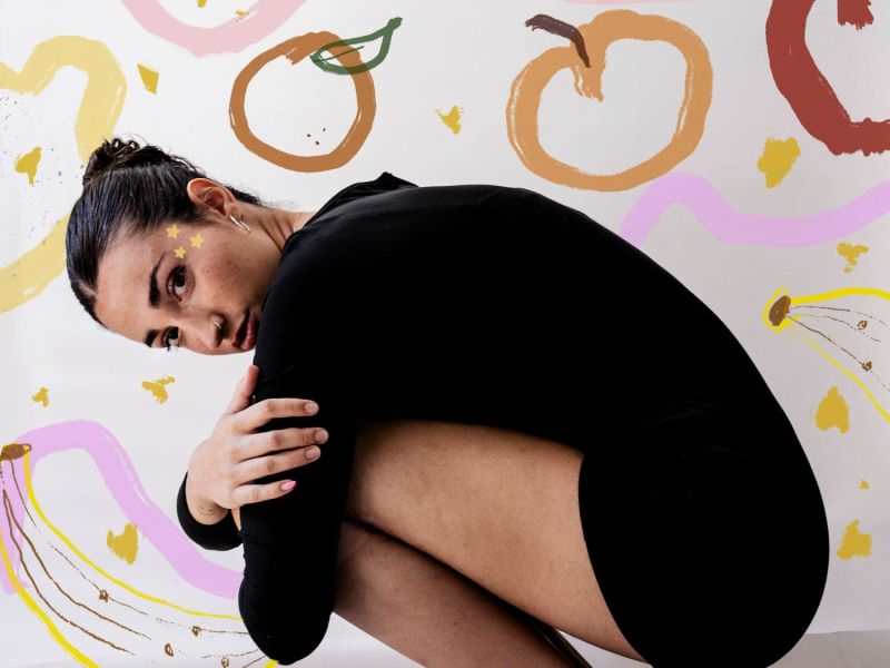 Frau hockt vor einer bunten Tapete.