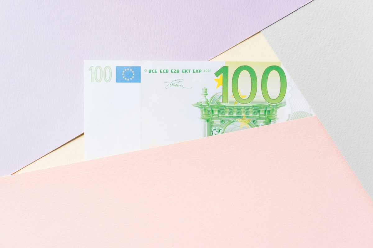 100-Euro-Geldschein auf pastellfarbenem Hintergrund.