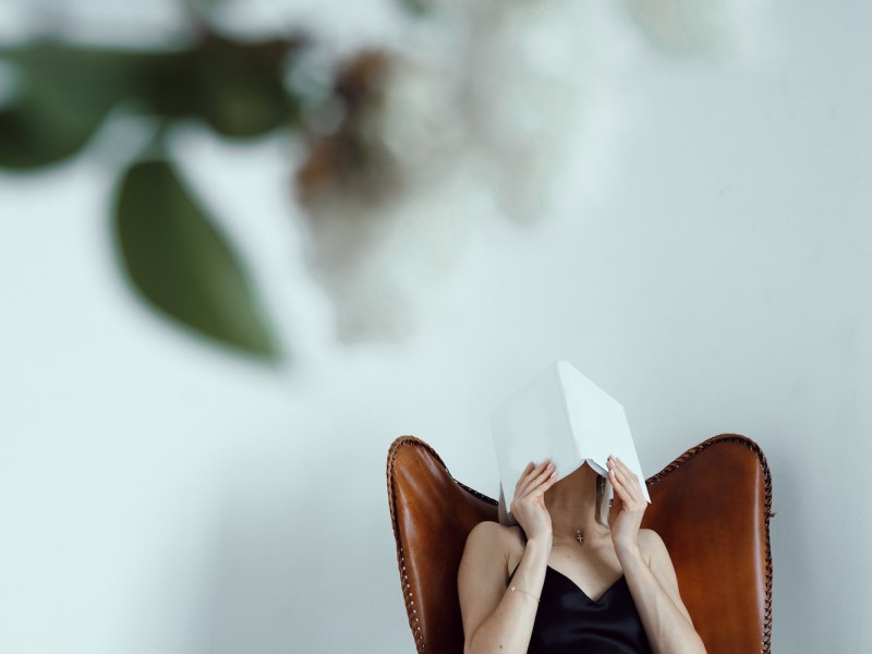 Eine Frau hält sich ein Buch vor das Gesicht.