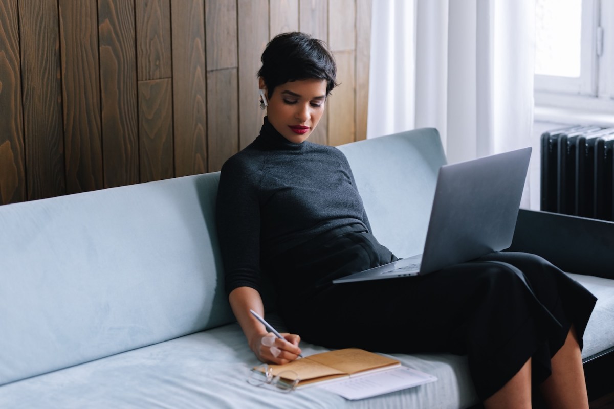 Frau sitzt auf einem Sofa und arbeitet an ihrem Laptop.