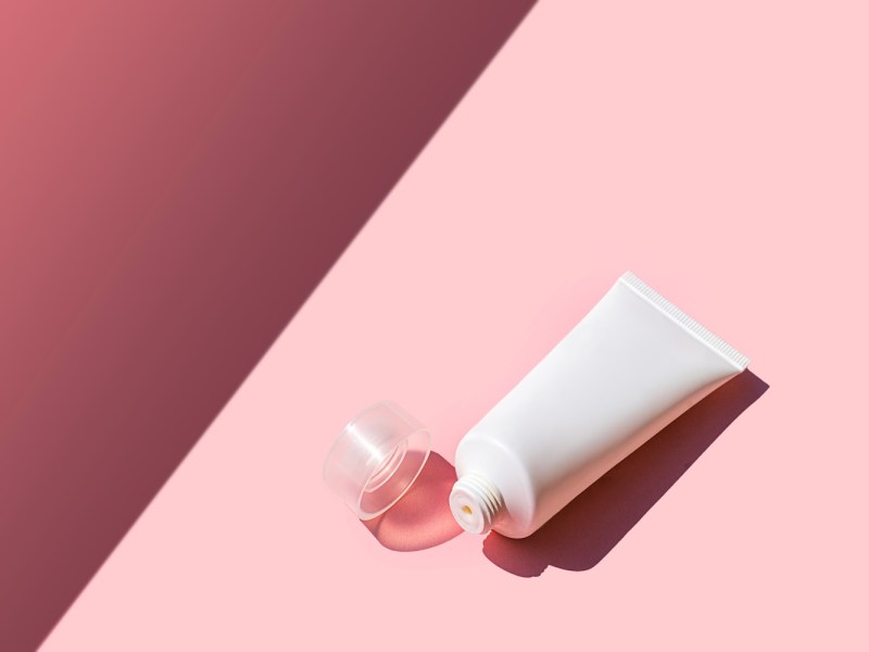 Kosmetikprodukt in weißer Kunststofftube auf rosa-magentafarbenem Hintergrund.