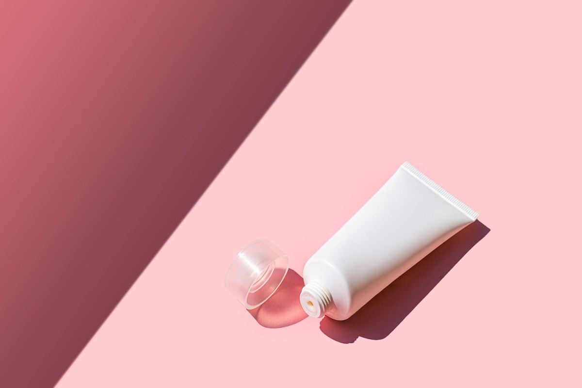 Kosmetikprodukt in weißer Kunststofftube auf rosa-magentafarbenem Hintergrund.